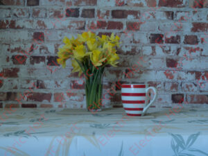 Table against brick wall with a daffodil and mug on it