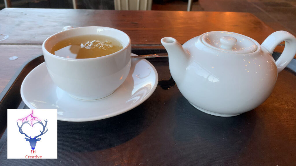 A steaming cup of tea and teapot in a cafe